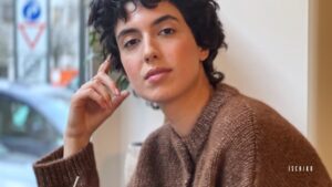 Person with dark curly hair in a brown sweater.